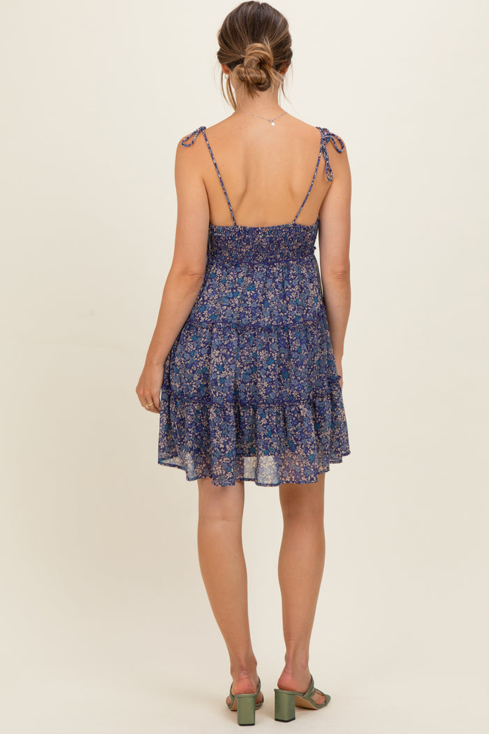 woman wearing a navy floral maternity dress with adjustable tie straps and a tiered skirt, showing a baby bump