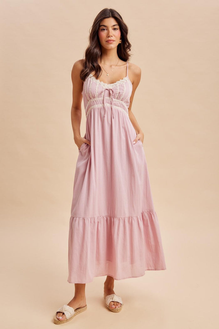 woman wearing a light pink maxi dress with adjustable straps, lace detailing, and pockets