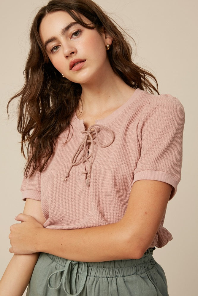 woman wearing a light pink short sleeve top with a lace-up neckline and rolled cuffs
