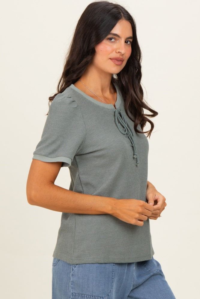 woman wearing a light green short sleeve top with a tie detail at the neckline and ribbed texture