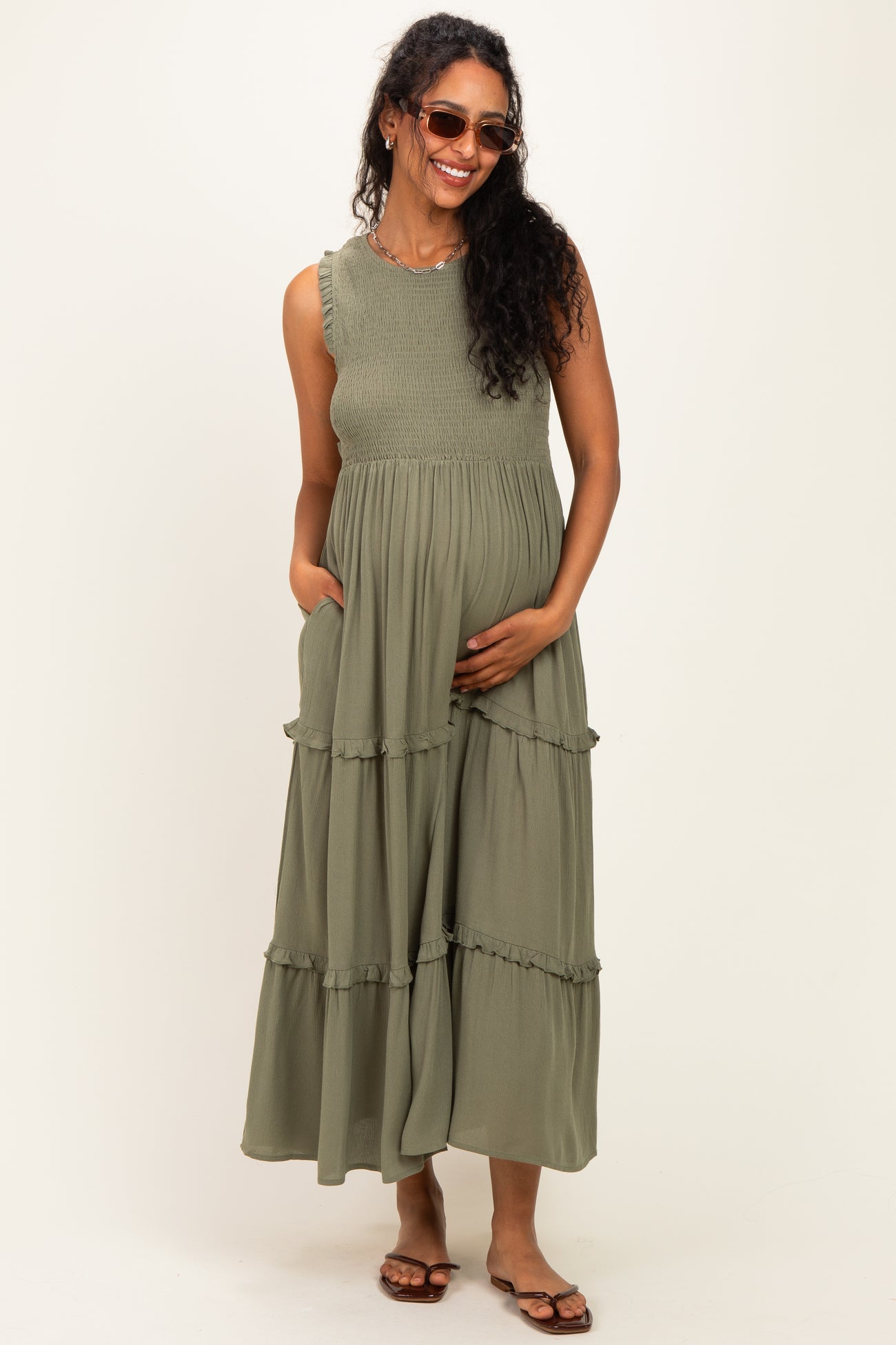 woman wearing a dark green maternity maxi dress with ruffle details and pockets, showcasing her baby bump