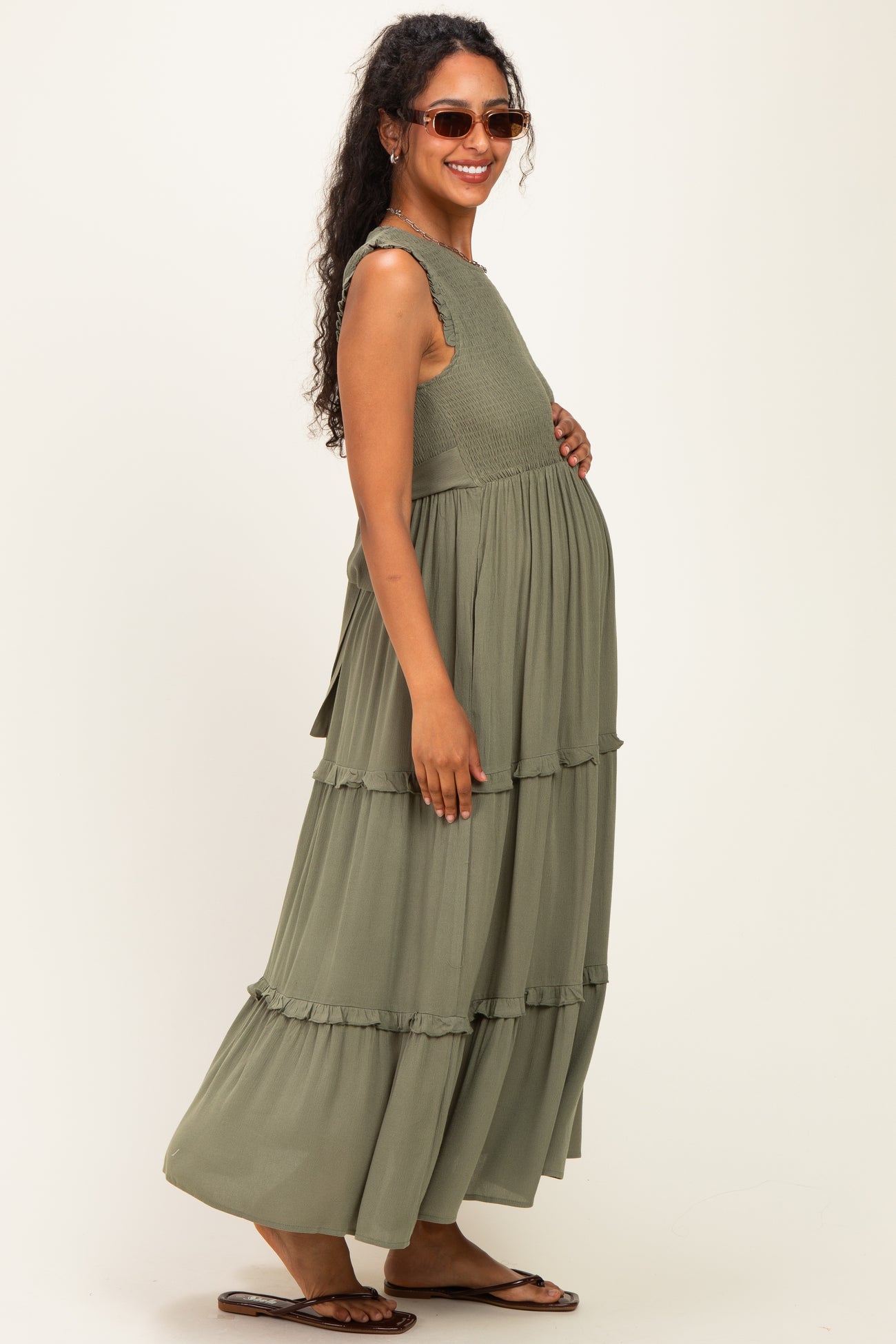 woman wearing a green tiered maternity maxi dress and showing her baby bump while smiling and wearing sunglasses
