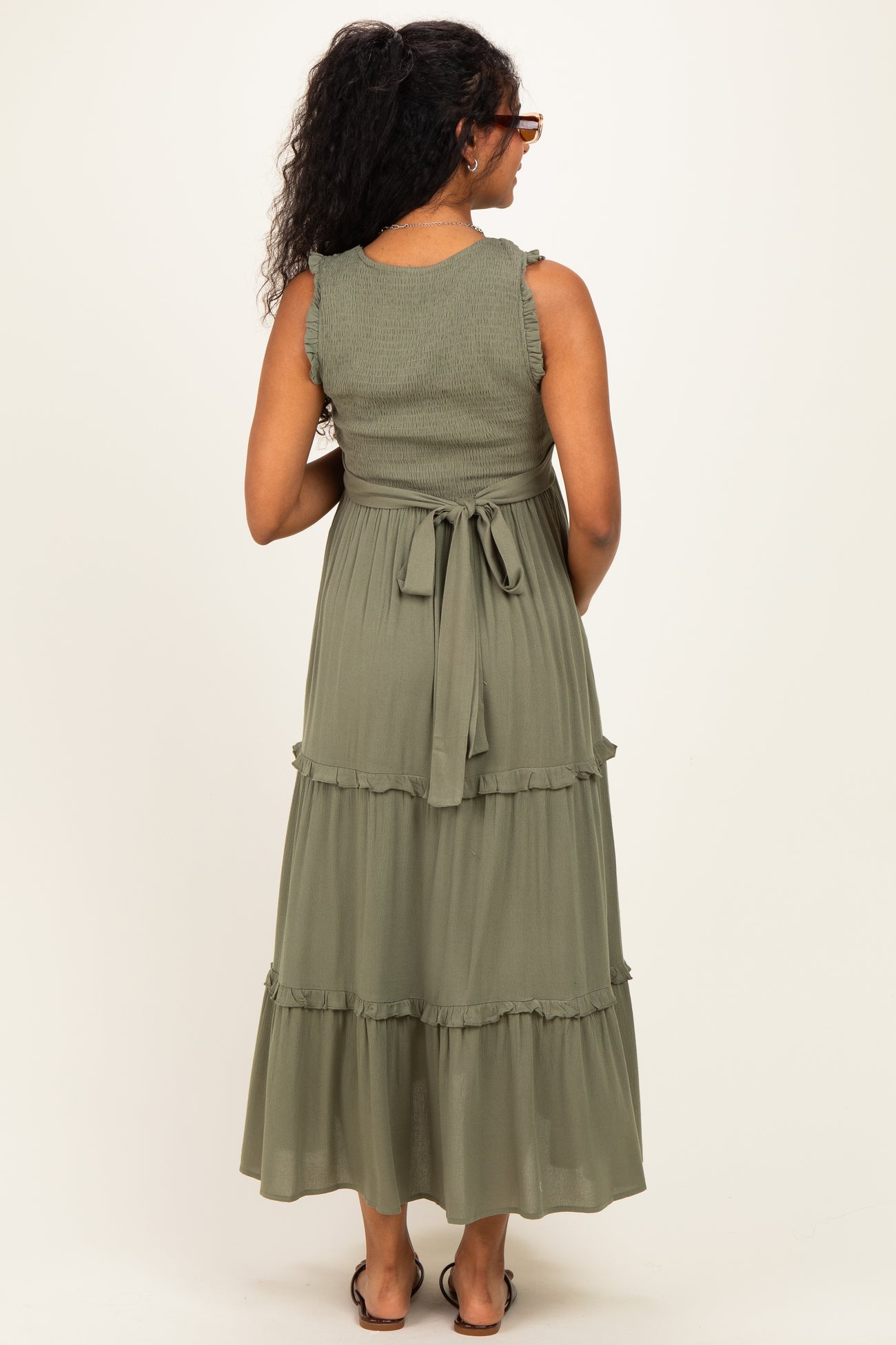 woman wearing a green tiered maternity dress with ruffled straps and a tied waist, showing a baby bump from behind