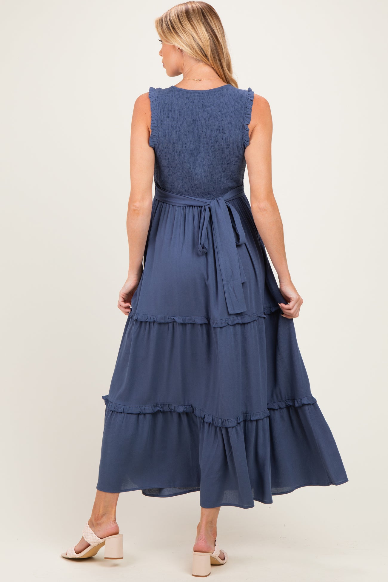 woman wearing a navy blue maternity maxi dress with ruffled tiers and a tied waist, viewed from the back