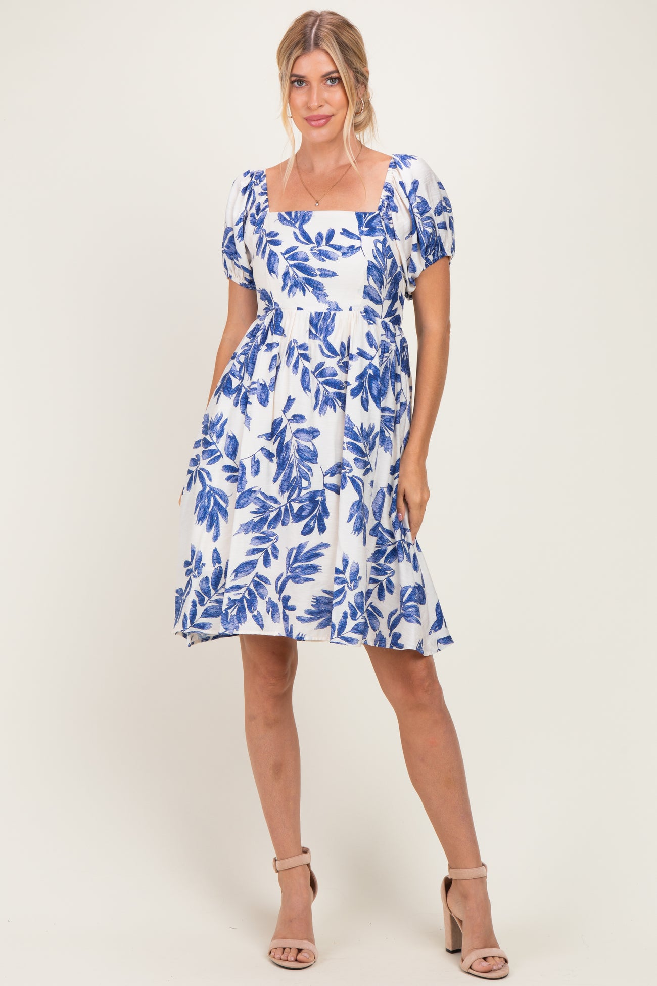 woman wearing a short puff sleeve white dress with blue floral print and a square neckline