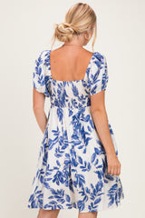 woman wearing a white dress with blue leaf print and short puff sleeves, shown from the back