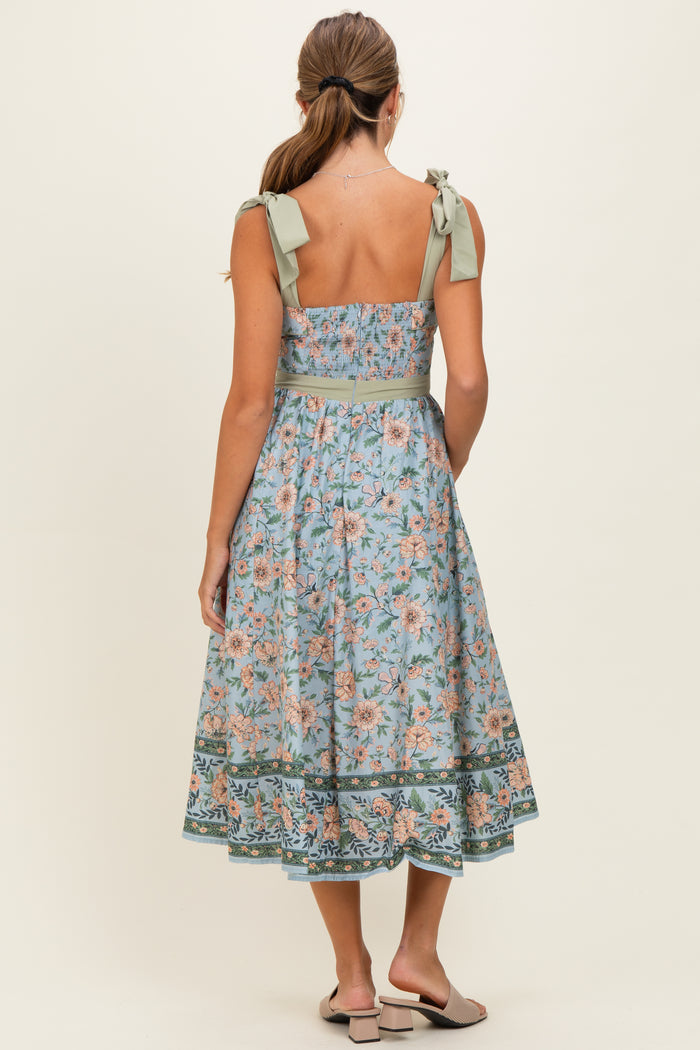woman wearing a floral print midi dress with a fitted bodice and tie straps in soft blue and pastel colors