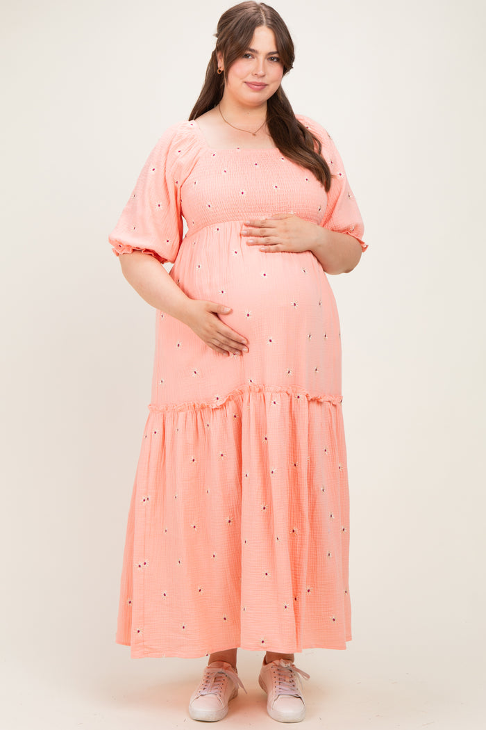 woman wearing a coral maternity dress with short puff sleeves and tiered skirt, holding her baby bump
