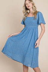 woman wearing a blue smocked midi dress with short puff sleeves and floral details.