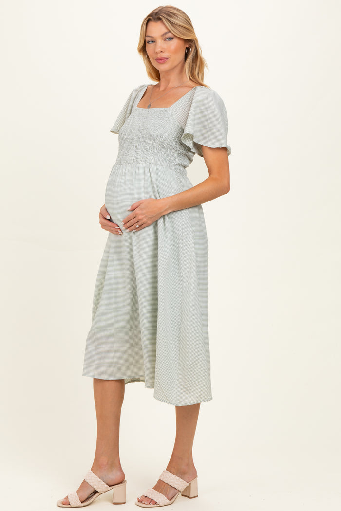 woman wearing a light green maternity dress with short puff sleeves and smocked bodice, holding her baby bump