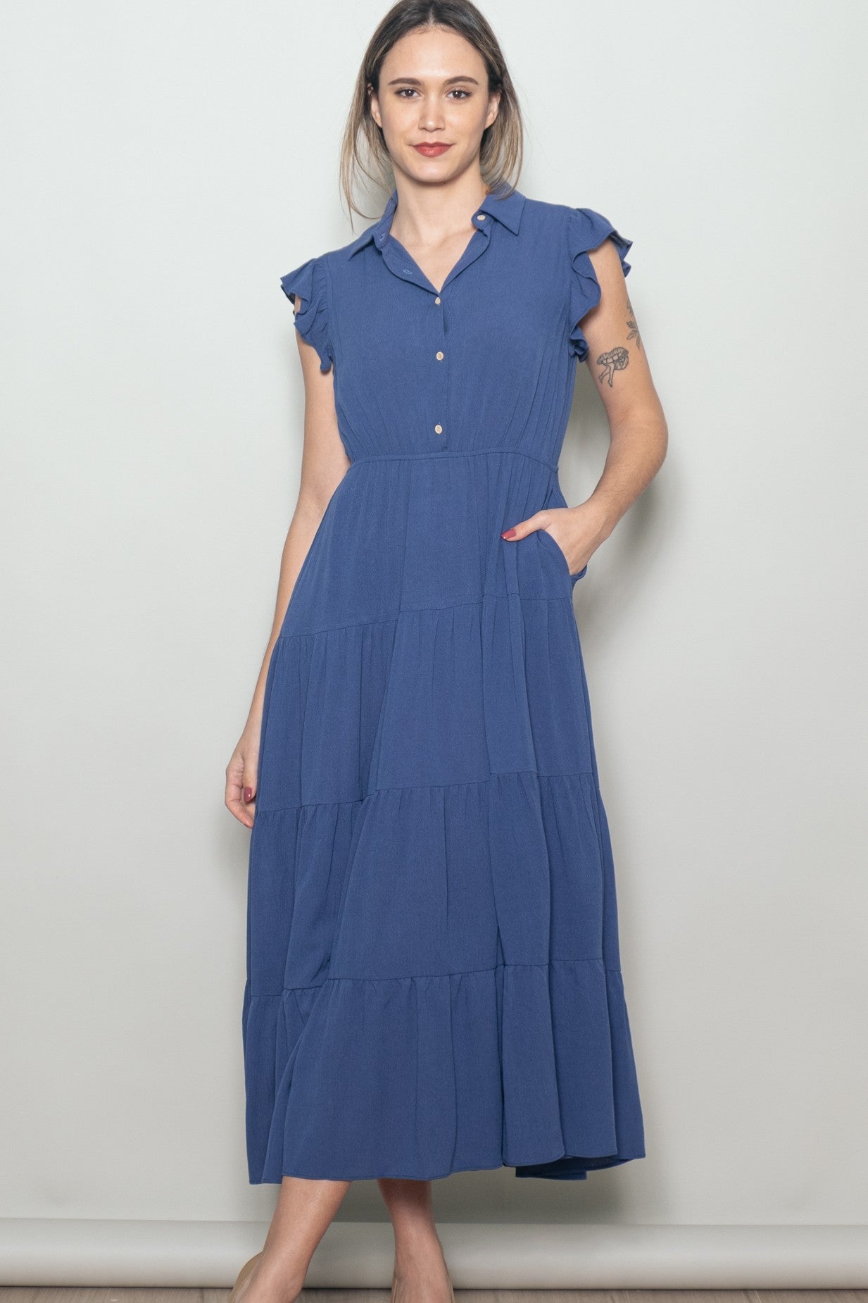 woman wearing a navy blue tiered midi dress with flutter sleeves and buttons down the front
