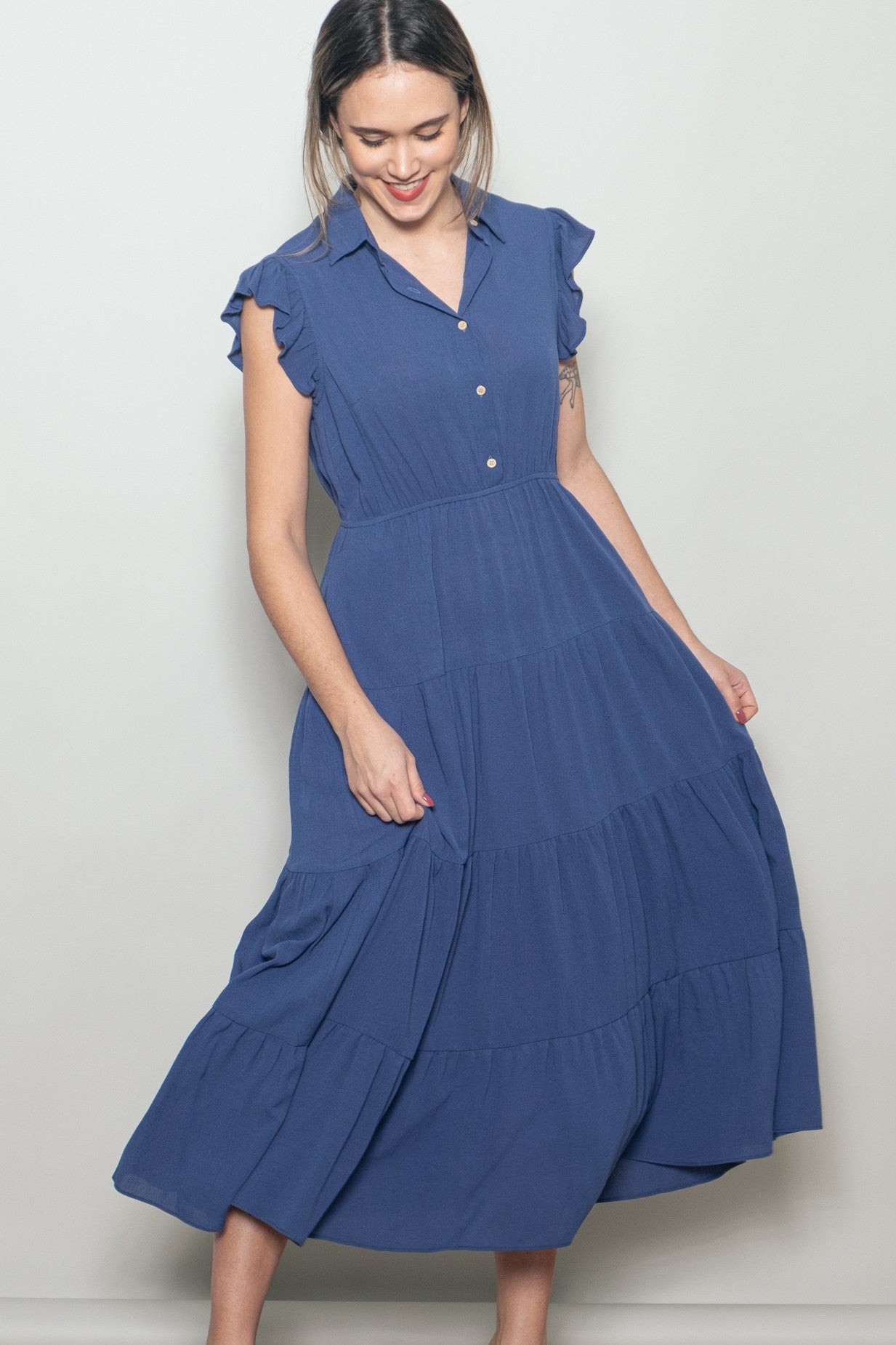 woman wearing a blue tiered midi dress with short ruffled sleeves and a button-up collar