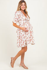 woman wearing a white floral maternity dress, smiling and cradling her baby bump