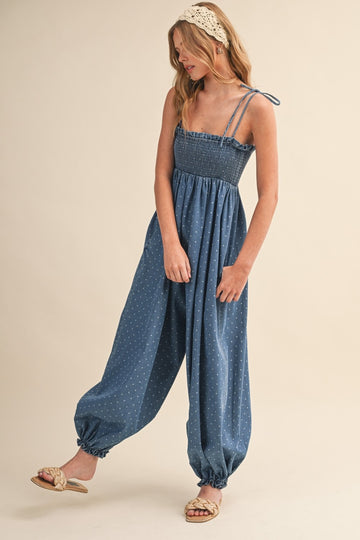 woman wearing a blue smocked jumpsuit with polka dots and adjustable straps, styled with flat sandals and a headband