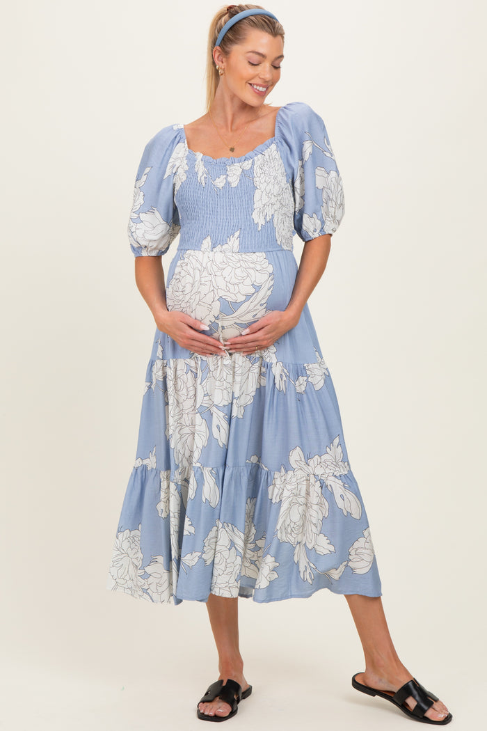 woman wearing a light blue floral maternity dress with puff sleeves, holding her baby bump