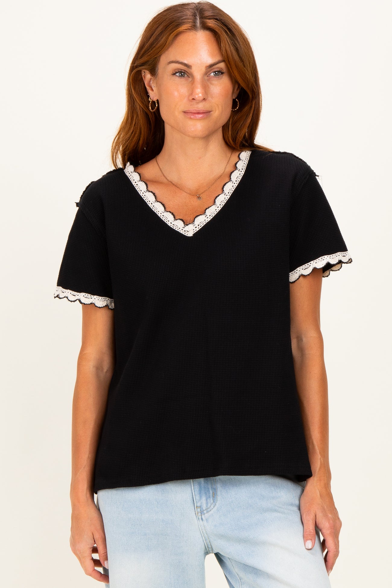 woman wearing a black ribbed short sleeve top with lace trim and a v-neckline paired with light blue jeans