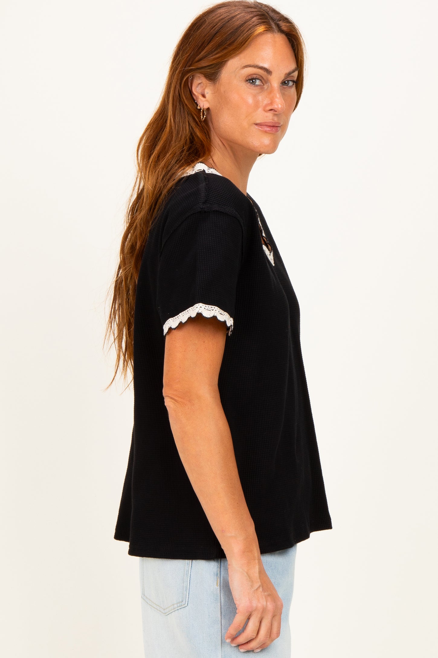 woman wearing a black short sleeve top with lace trim and a relaxed fit, styled with light blue jeans