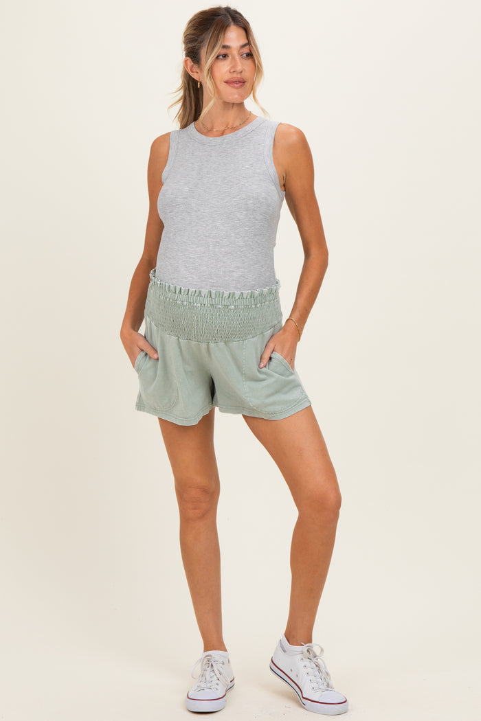 woman wearing a gray sleeveless maternity top and green smocked maternity shorts with side pockets