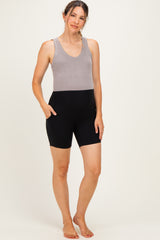 woman wearing a gray tank top and black maternity bike shorts with pockets, standing barefoot on a light background