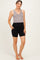 woman wearing a gray tank top and black maternity bike shorts with pockets, standing barefoot on a light background