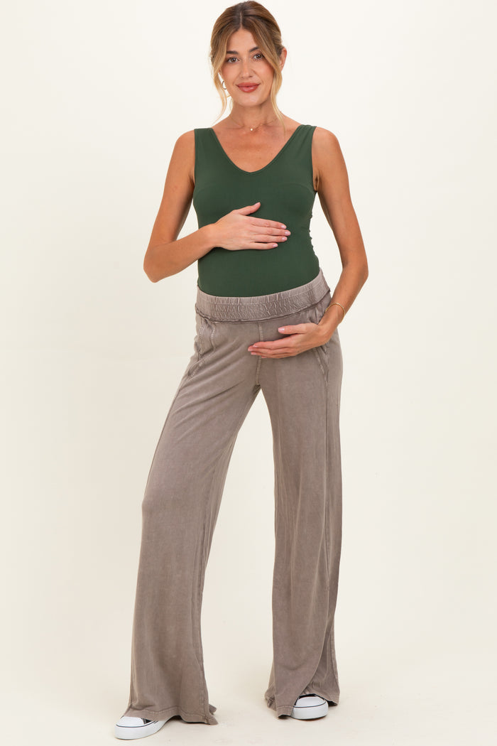 woman wearing a green sleeveless maternity top and beige wide-leg maternity pants, holding her baby bump