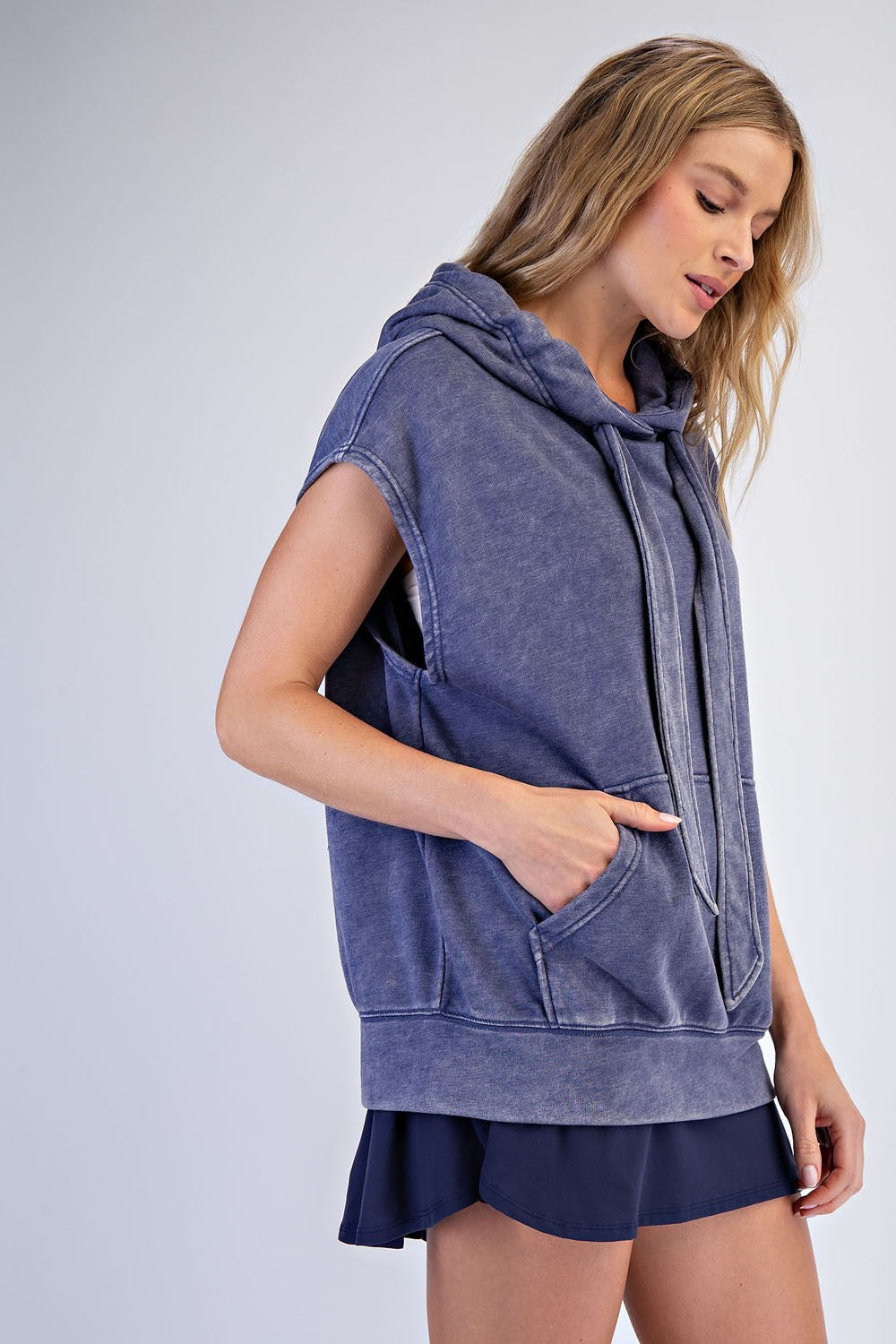 woman wearing a dark blue sleeveless hooded sweatshirt with a front pocket and a relaxed fit