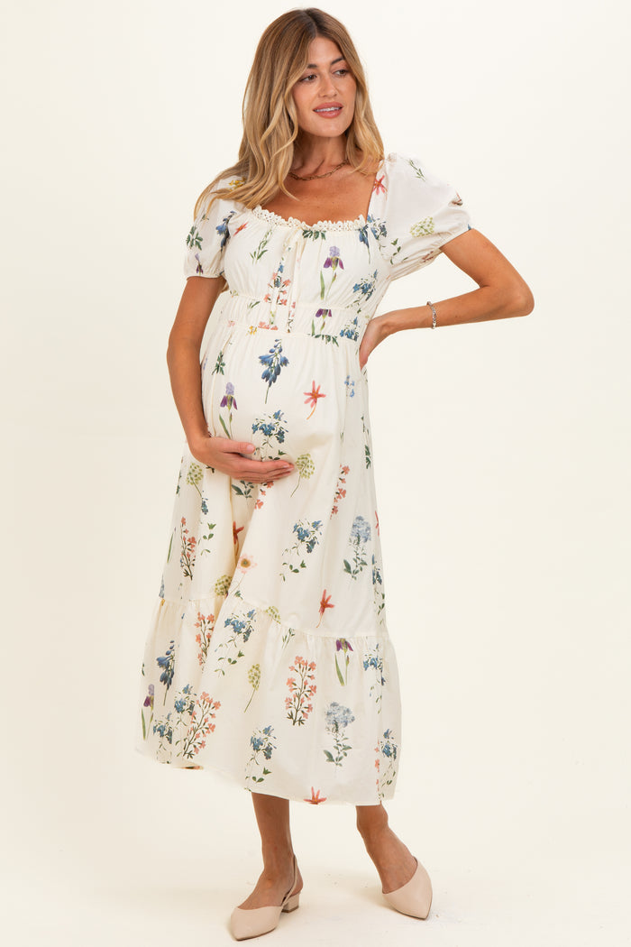 woman wearing a white floral maternity maxi dress and holding her baby bump