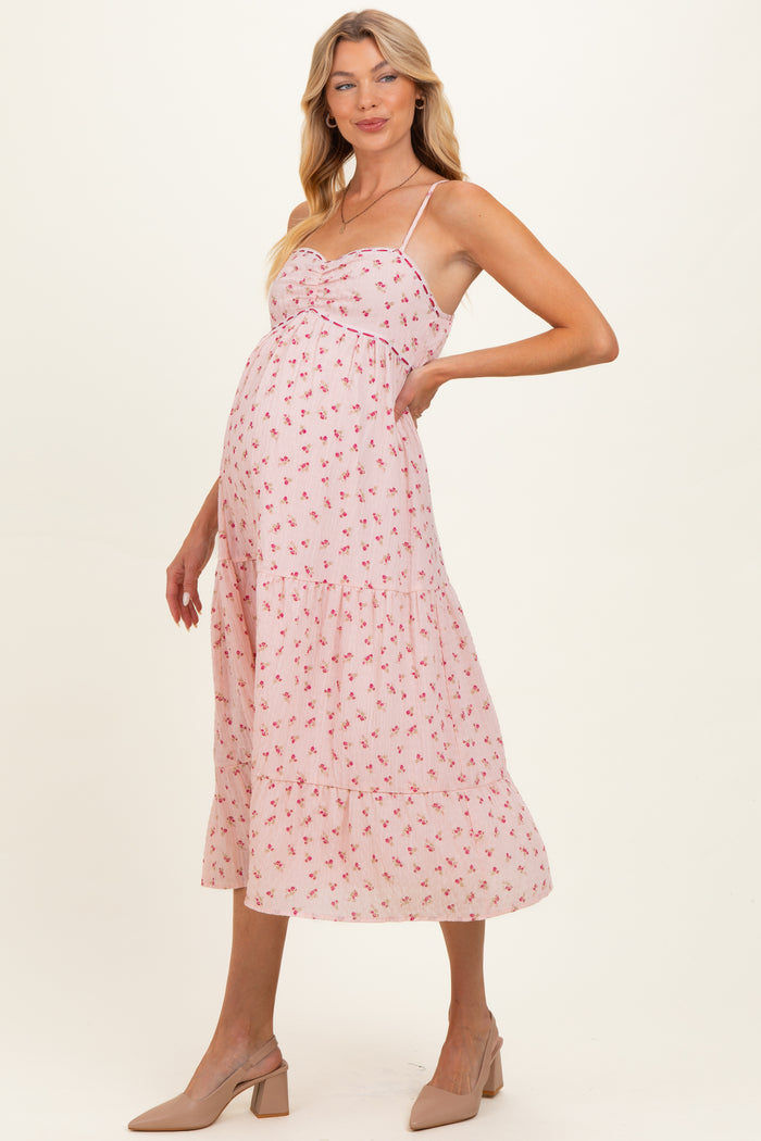 woman wearing a pink floral maternity dress with a tiered skirt and adjustable straps, highlighting her baby bump