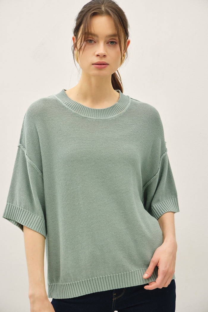 woman wearing a loose-fitting, light green short-sleeve sweater with a round neckline and ribbed detailing
