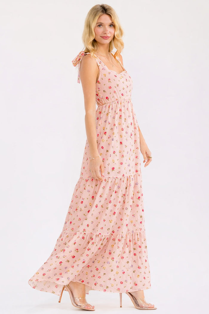 woman wearing a light pink floral maxi dress with tie straps and a tiered skirt