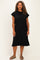 woman wearing a relaxed black short sleeve plus size dress with side slits and standing against a neutral background