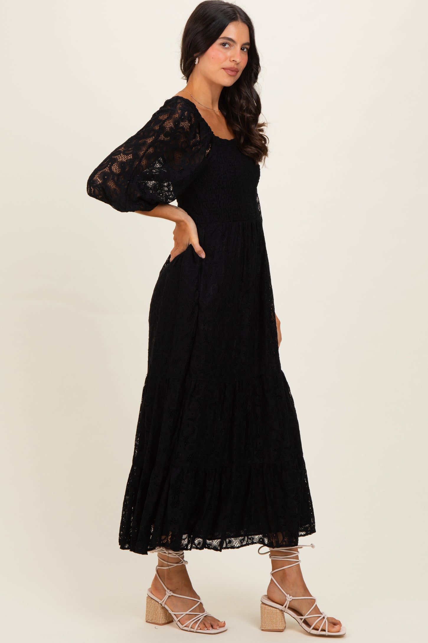 woman wearing a black lace long sleeve maxi dress and strappy sandals standing in profile
