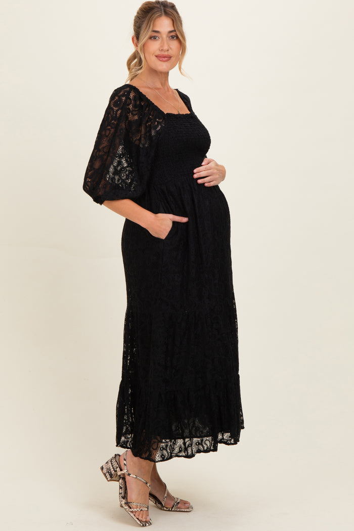woman wearing a black lace maternity dress with puff sleeves and pockets, cradling her baby bump
