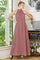 woman wearing a blush pink halter neck maxi dress standing by a window with greenery in the background
