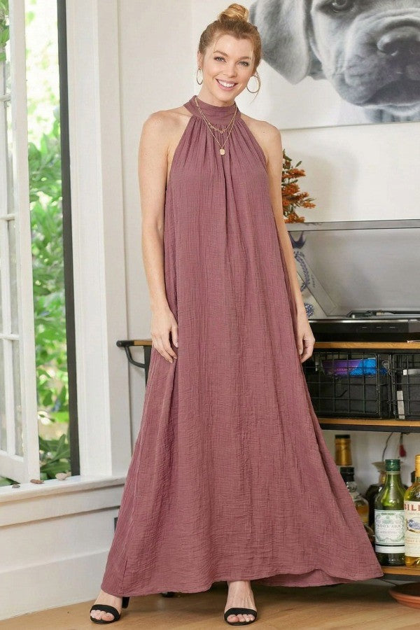 woman wearing a mauve halter neck maxi dress with a flowy silhouette and a layered necklace, standing indoors