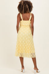 woman wearing a yellow lace maternity dress with ruffled straps and a flared skirt, showing a baby bump from the back
