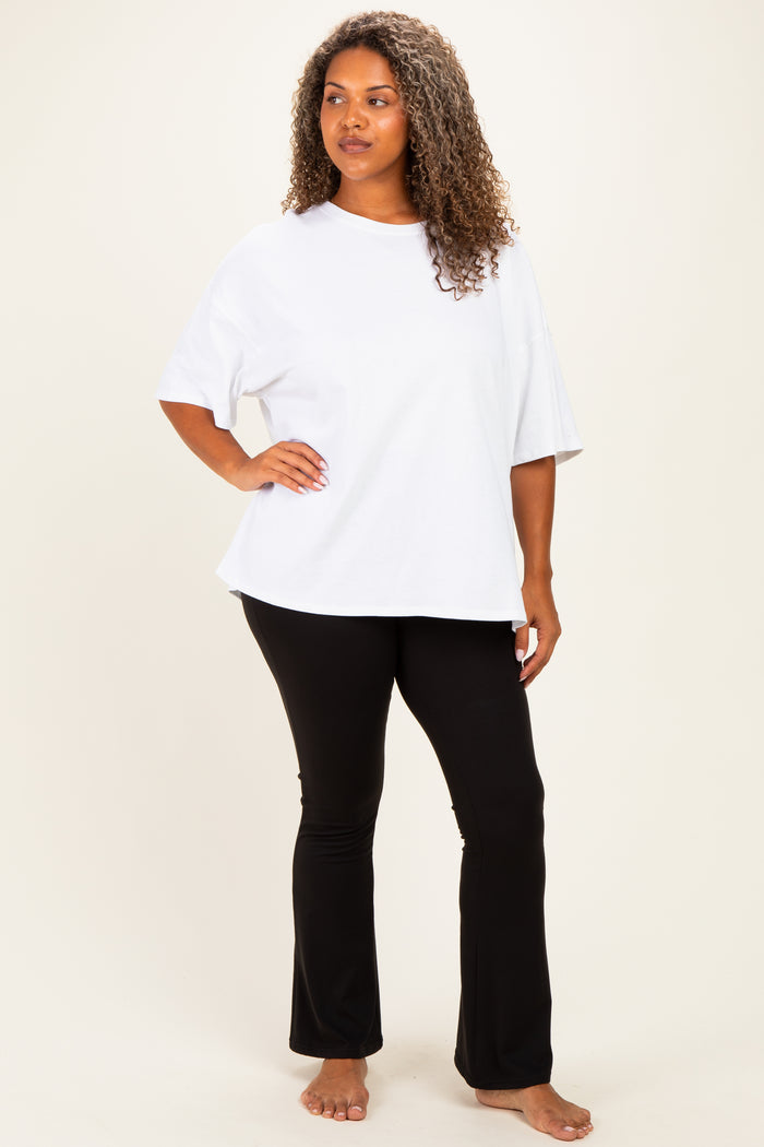 woman wearing a white oversized t-shirt and black flared pants, standing barefoot against a light background