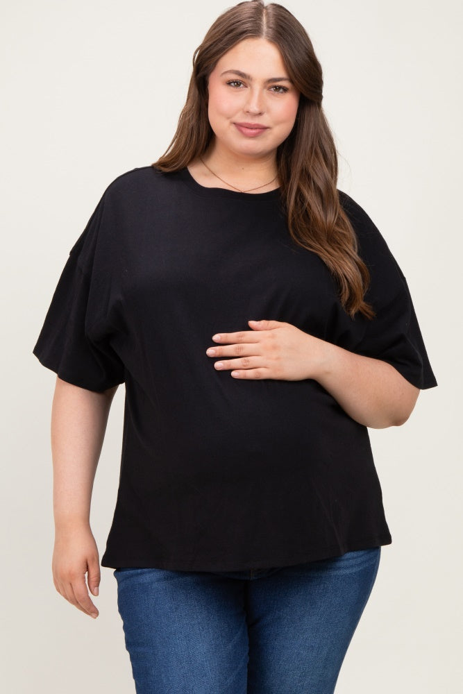 woman wearing a black oversized maternity top and holding her baby bump