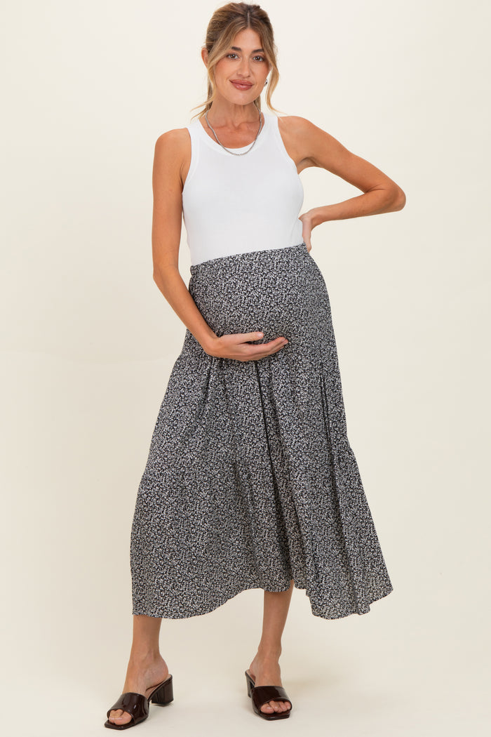 woman wearing a white tank top and a black floral maternity skirt, holding her baby bump