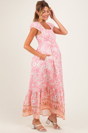 woman wearing a pink floral maxi maternity dress with cap sleeves and pockets, showing her baby bump