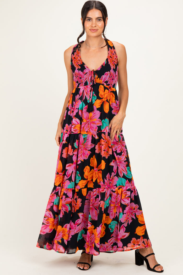 woman wearing a black floral maxi dress with vibrant pink and orange flowers and a tiered skirt, posing with one hand on her hip