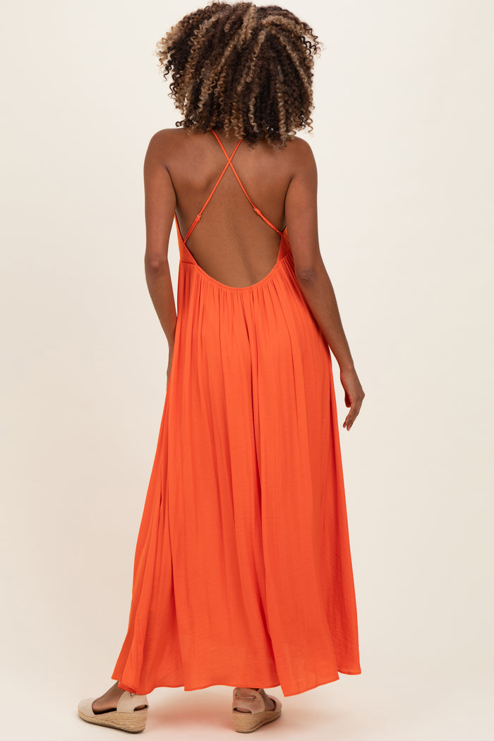 woman wearing an orange backless maternity maxi dress with crisscross straps and flowing silhouette