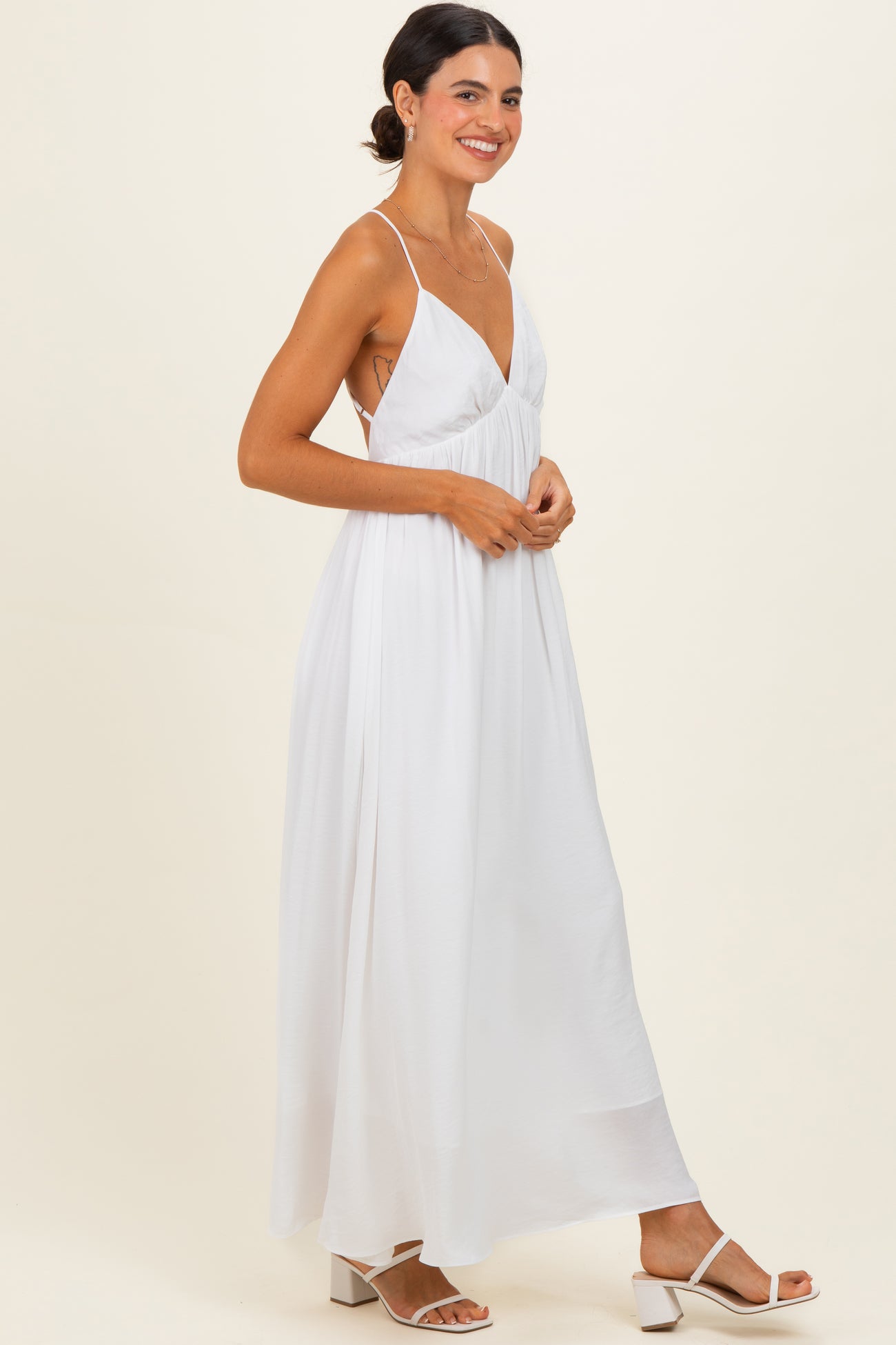 woman wearing a white maxi dress with a v-neck and spaghetti straps, standing and smiling