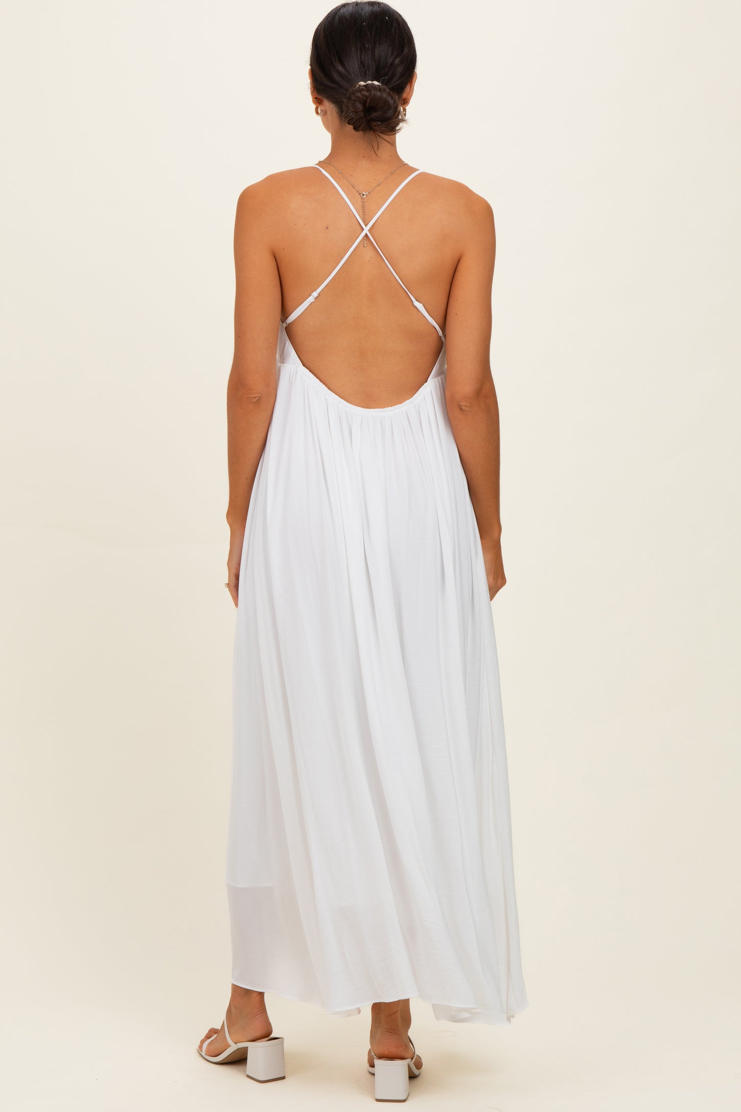 woman wearing a white backless maxi dress with crisscross straps and a flowy silhouette