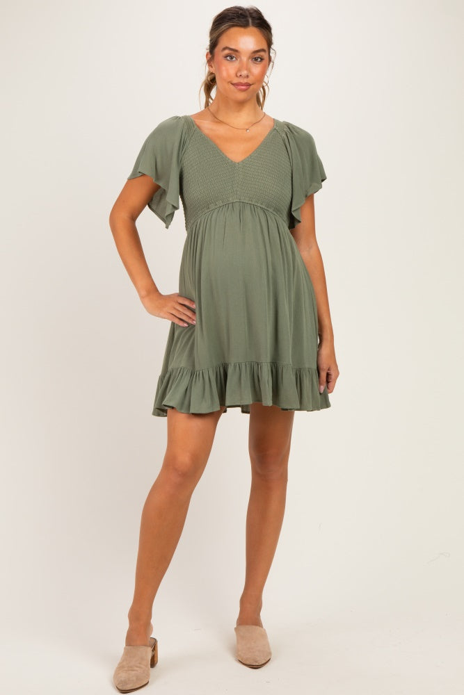 woman wearing a green short sleeve maternity dress with a smocked bodice and ruffled hem, showing her baby bump