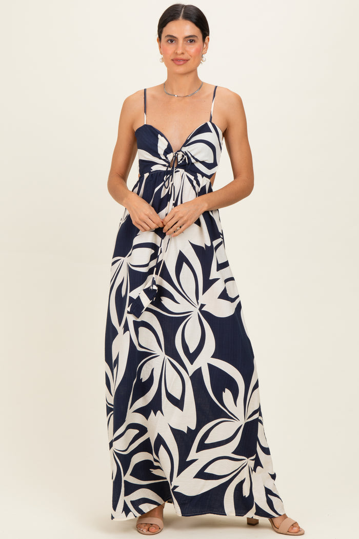 woman wearing a navy blue and white floral print maxi dress with a front tie detail and spaghetti straps