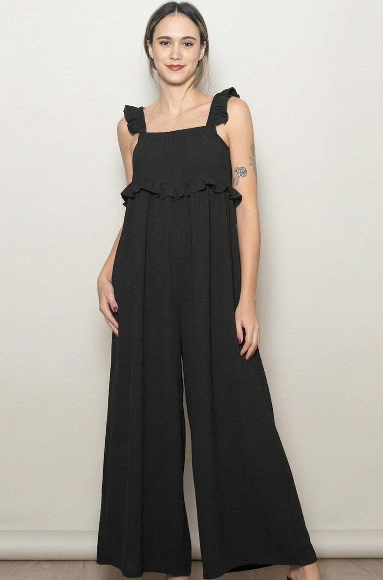 woman wearing a black sleeveless jumpsuit with ruffle details and wide legs