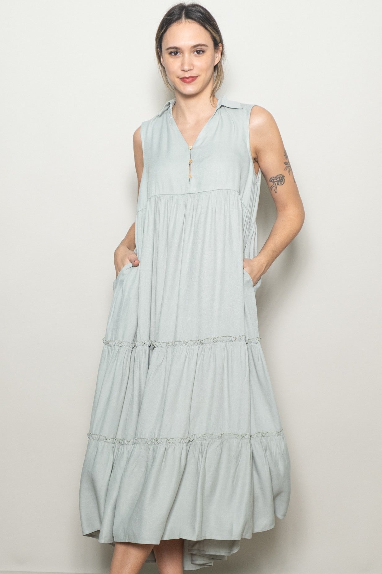 woman wearing a light green sleeveless tiered midi dress with a collared neck and side pockets