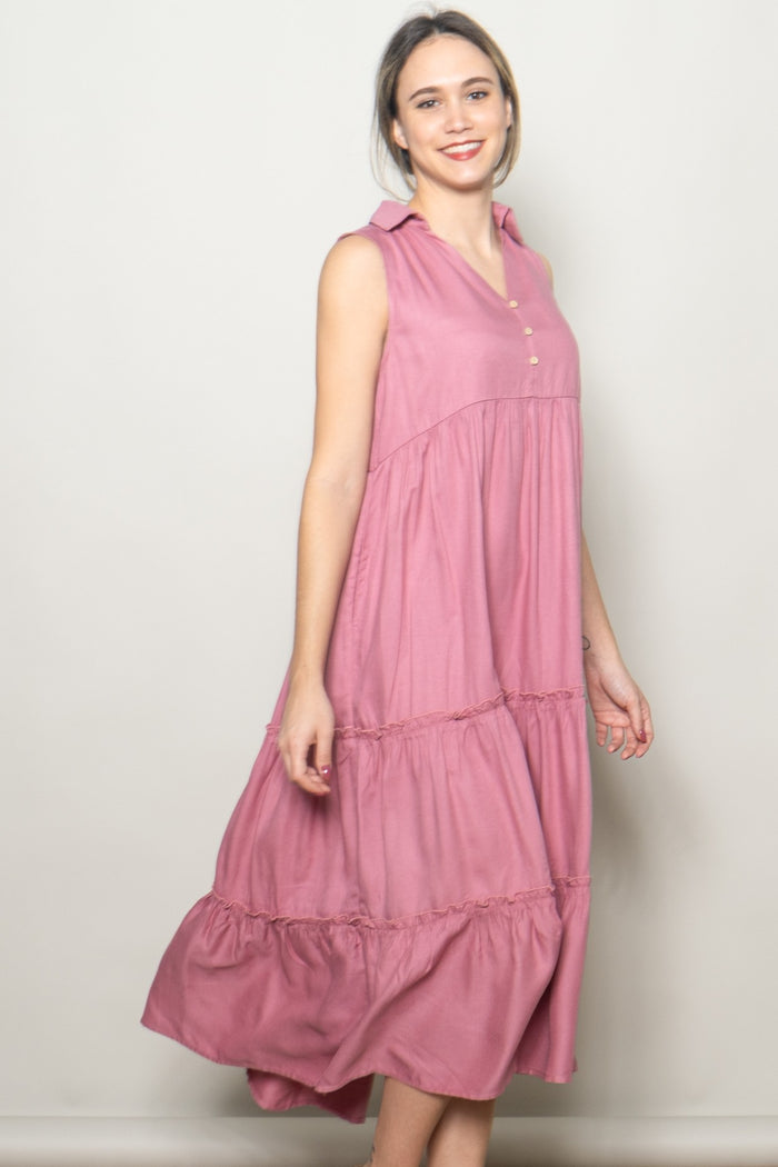woman wearing a pink sleeveless tiered midi dress with buttons and a collared neckline