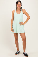woman wearing a light green sleeveless casual dress with side pockets and black athletic shoes